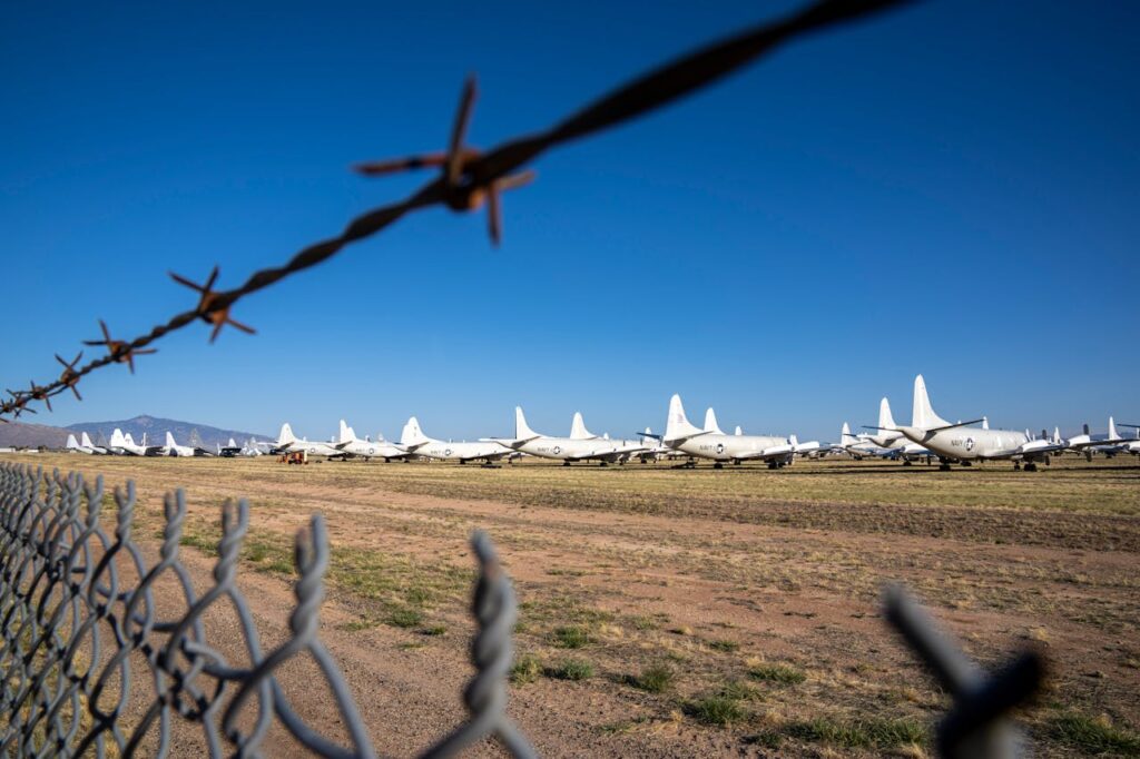 The Art of Drawing Readers In: Your attractive post title goes here Airplane boneyard viewed through barbed wire fence under clear blue sky.